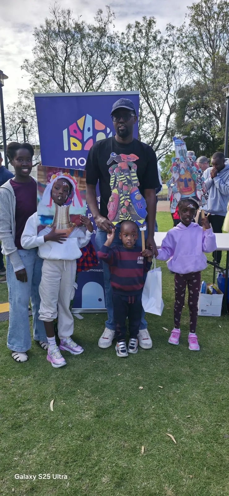 A KENEWA family at the Mosaic Multicultural Connections stand, the children with painted faces holding up colourful masks