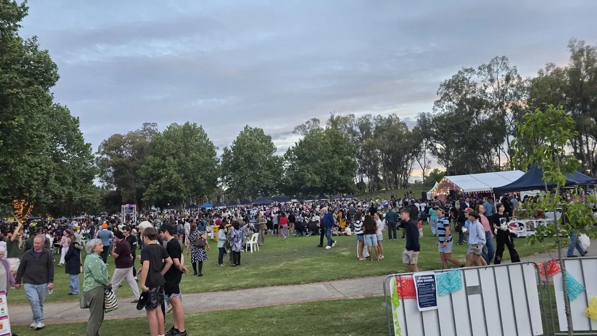 A wide view of the busy festival lawn at Fiesta La Peel, with rows of stall tents and a lit stage
