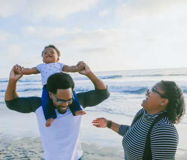A family on a beach, a baby on his father's shoulders
